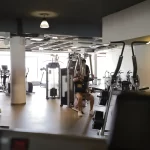 Interior do ginásio com clientes a usar máquinas de exercício e pesos