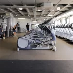 Interior do ginásio com máquinas de exercício e pessoas a realizar exercicios